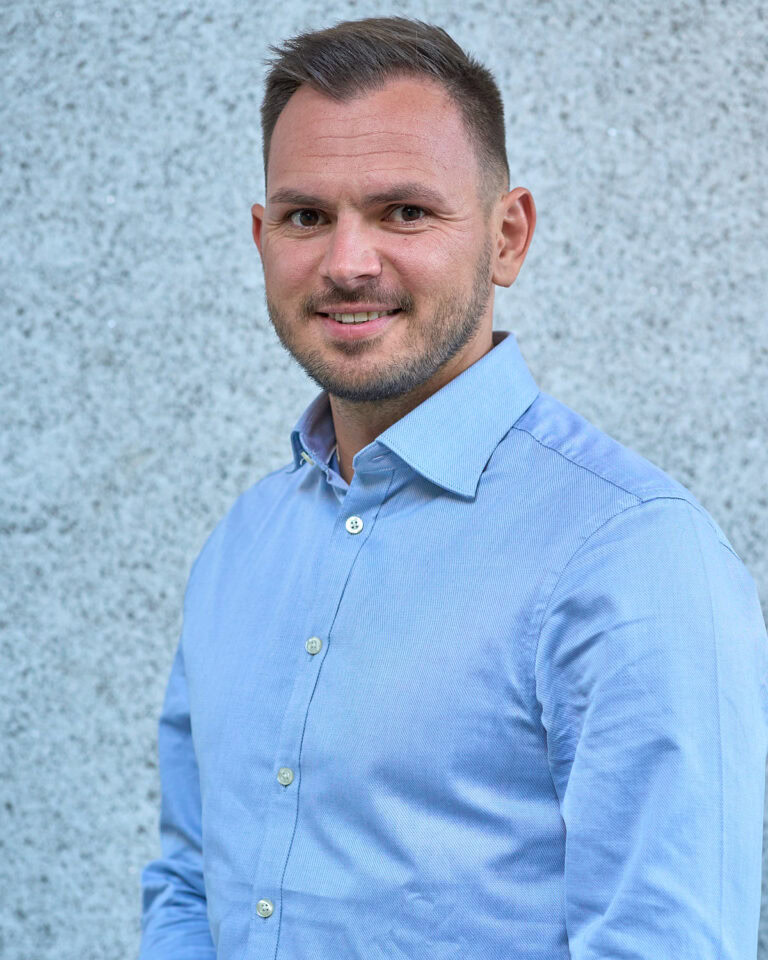 Smiling man with beard in light blue button-down shirt.